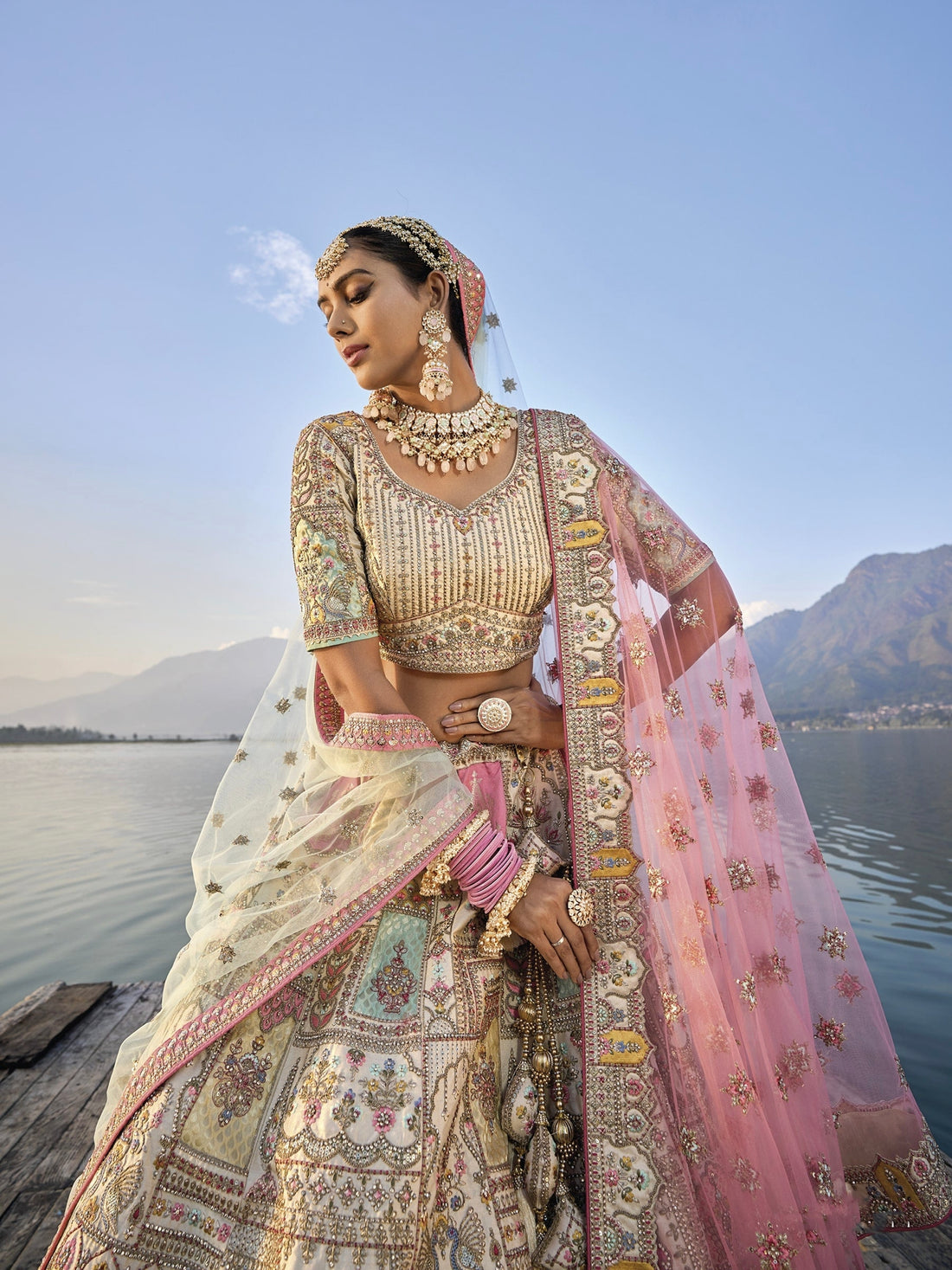 Woman in off-white silk lehenga with embroidered peach dupatta by a lake.