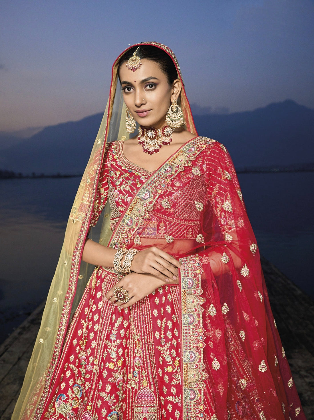 Woman in red silk lehenga with embroidered net dupatta by a lake.