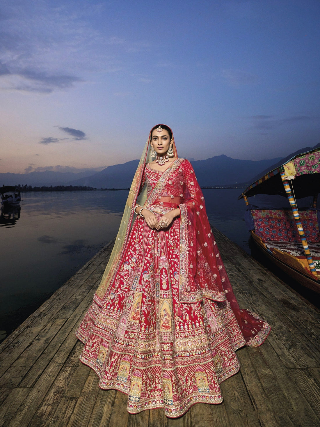 Woman in red silk lehenga with embroidered net dupatta by a lake.