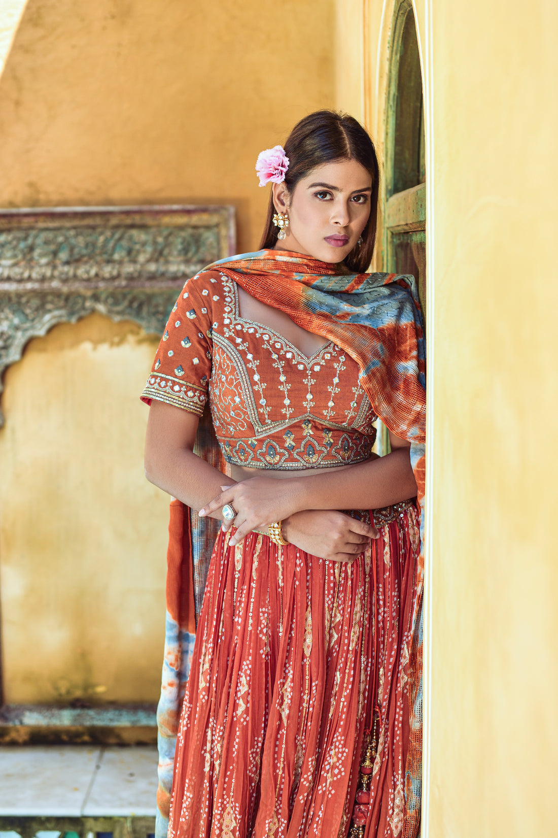 Woman wearing orange lehenga choli with digital print, mirror work, and sequence embellishments.